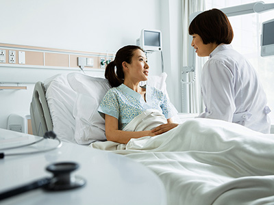 Female doctor sitting on hospital bed and discussing with young female patient