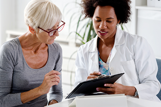 A female doctor sits at her desk and chats to an elderly female patient while looking at her test results